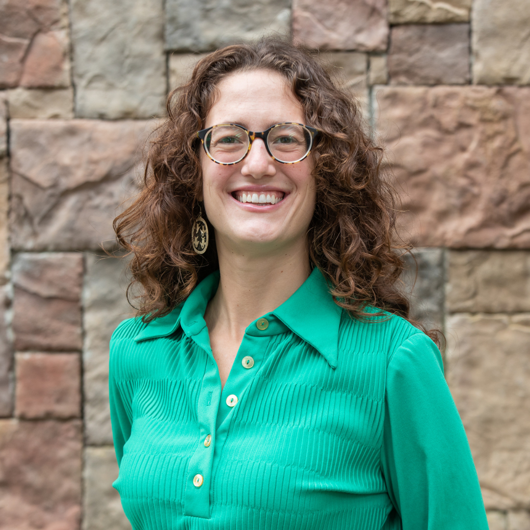 Laura poses for a headshot in front of a brick wall