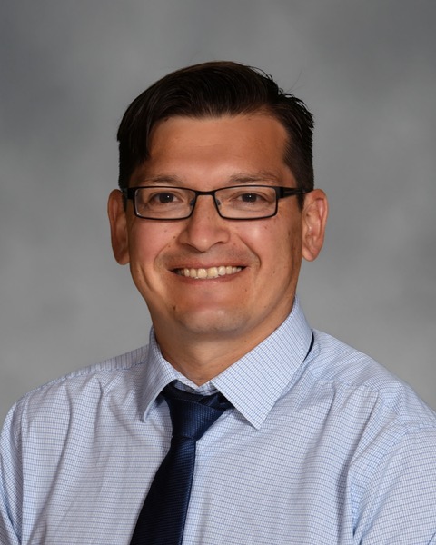 César Cordova poses for a headshot in front of a gray background 