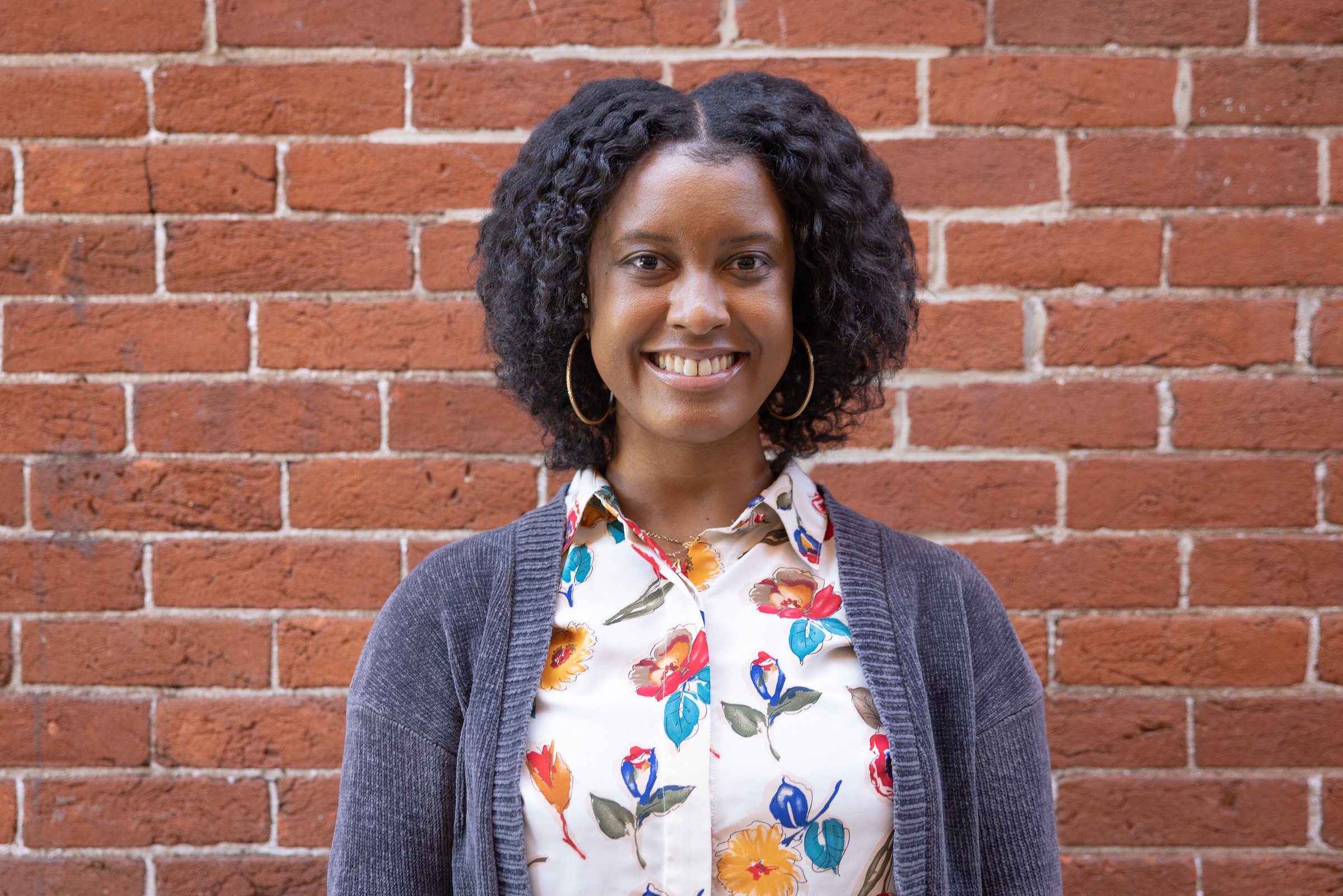 Bria Drews poses for headshot in front of a brick wall