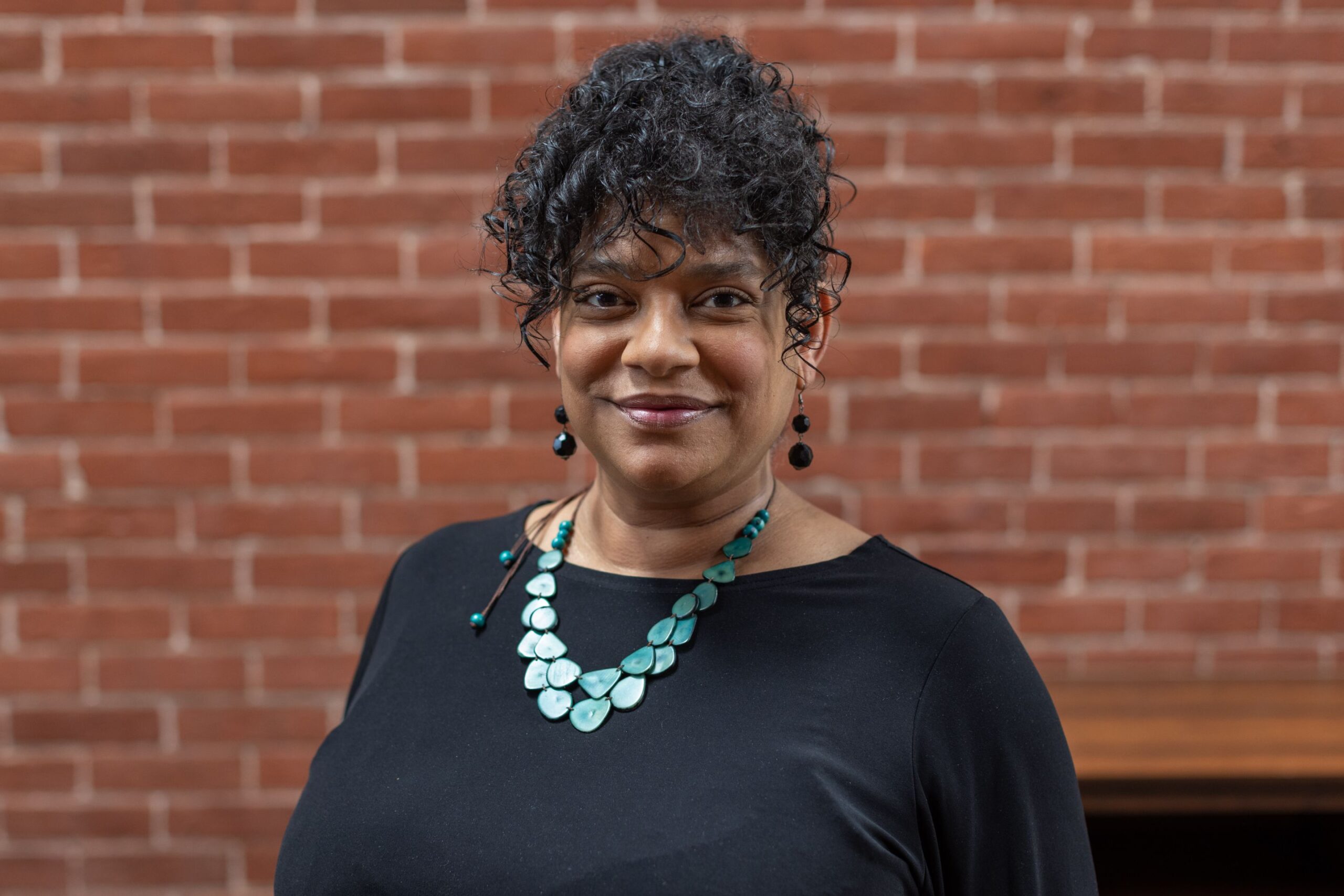 Woman in front of brick wall stands facing the camera.